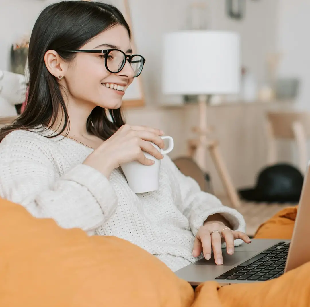 Mladá žena pije kávu a spokojeně se dívá na notebook v obývacím pokoji